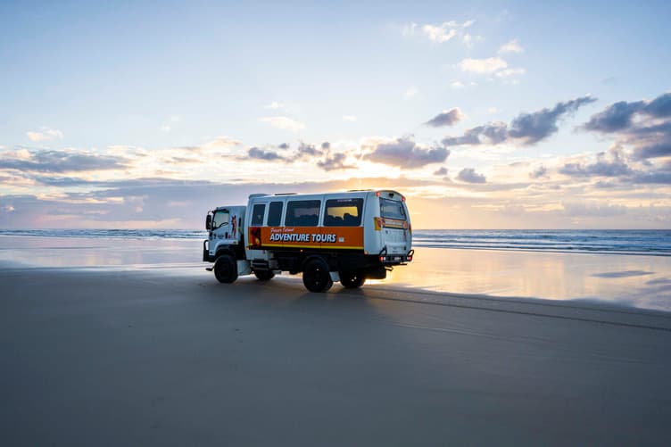 A tour vehicle driving along the beach with the ocean behind it