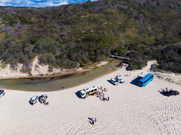 A group of vehicles on a white sandy area next to a creek