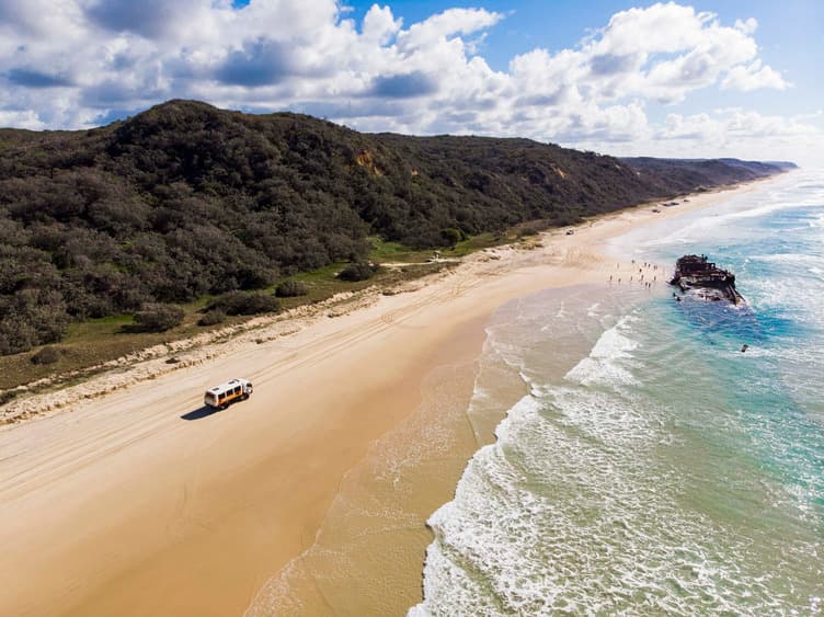 A shipwreck on a beach surrounded by a tour group with a tour vehicle on the sand