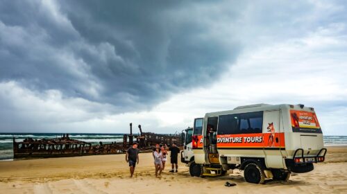 Tour vehicle parked in front of a shipwreck on a beach