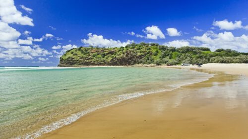 A sandy beach with a large hill and some tour vehicles in the background