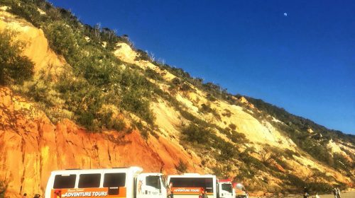 Large cliffside with tour vehicles parked at the base